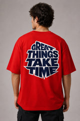 Male model wearing a red oversized t-shirt with 'Believe' printed in navy blue and white collegiate-style lettering.
