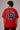 Male model wearing a red oversized t-shirt with 'Believe' printed in navy blue and white collegiate-style lettering.