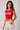 Back view of a woman wearing a red Coco-Cola crop top with white trim and beige high-waisted pants against a white background.
