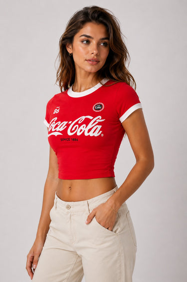 Back view of a woman wearing a red Coco-Cola crop top with white trim and beige high-waisted pants against a white background.