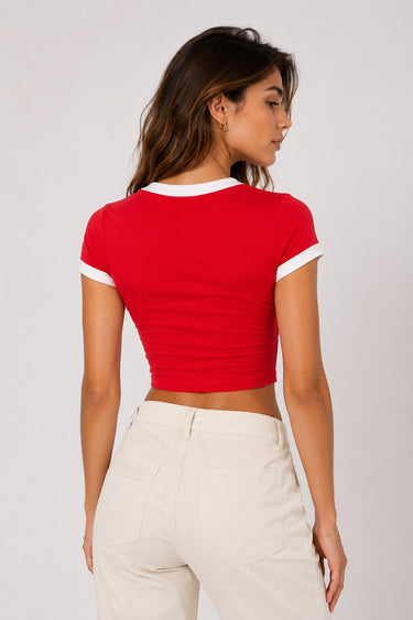 Back view of a woman wearing a red Coco-Cola crop top with white trim and beige high-waisted pants against a white background.