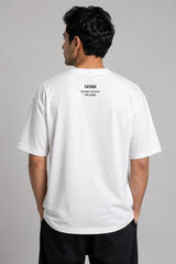 Man wearing a white oversized FAKR t-shirt with a graphic design of the word "Fakr" integrated with superhero symbols, on a plain gray background.
