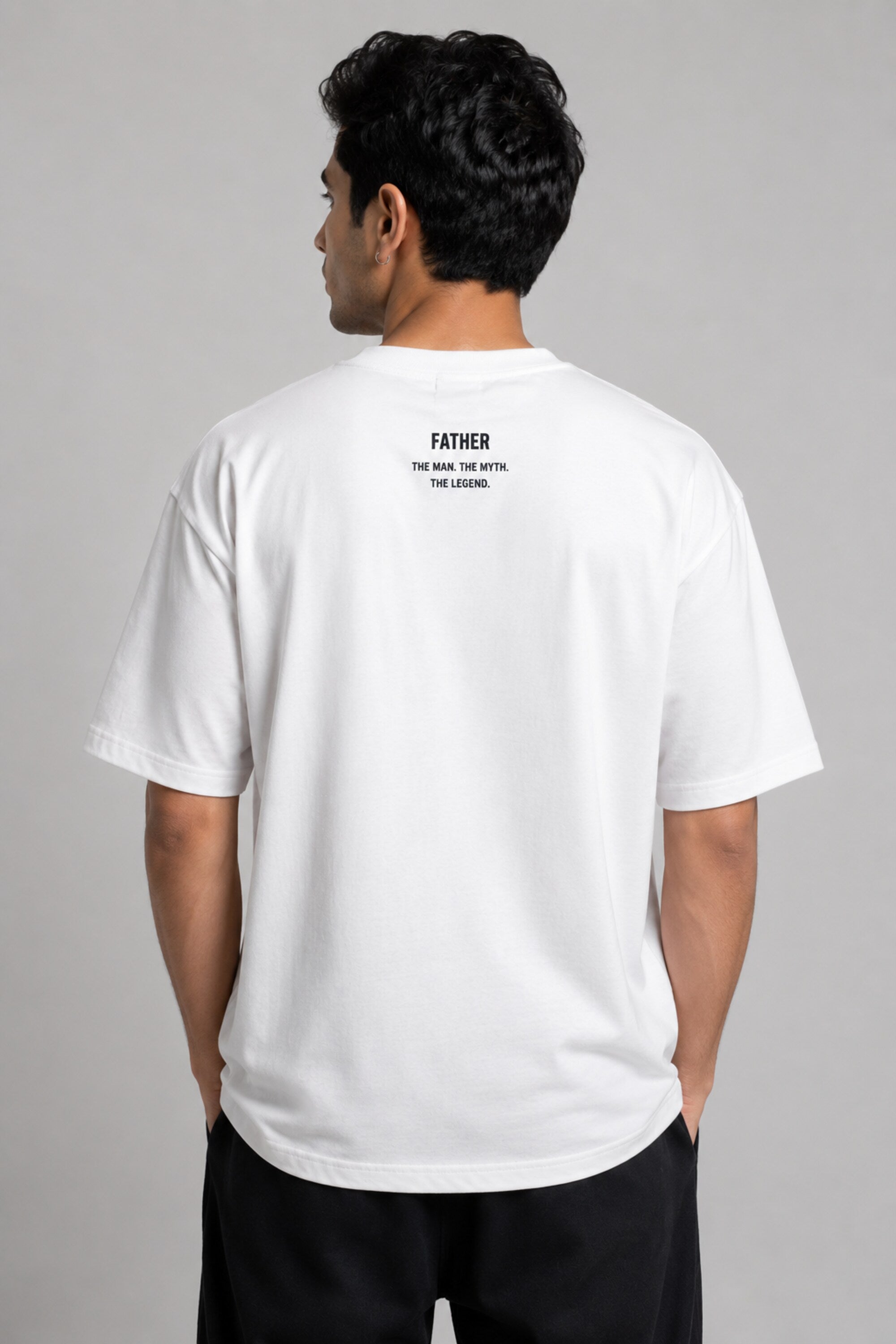 Man wearing a white oversized FAKR t-shirt with a graphic design of the word "Fakr" integrated with superhero symbols, on a plain gray background.