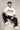Man wearing a white oversized FAKR t-shirt with a graphic design of the word "Fakr" integrated with superhero symbols, on a plain gray background.