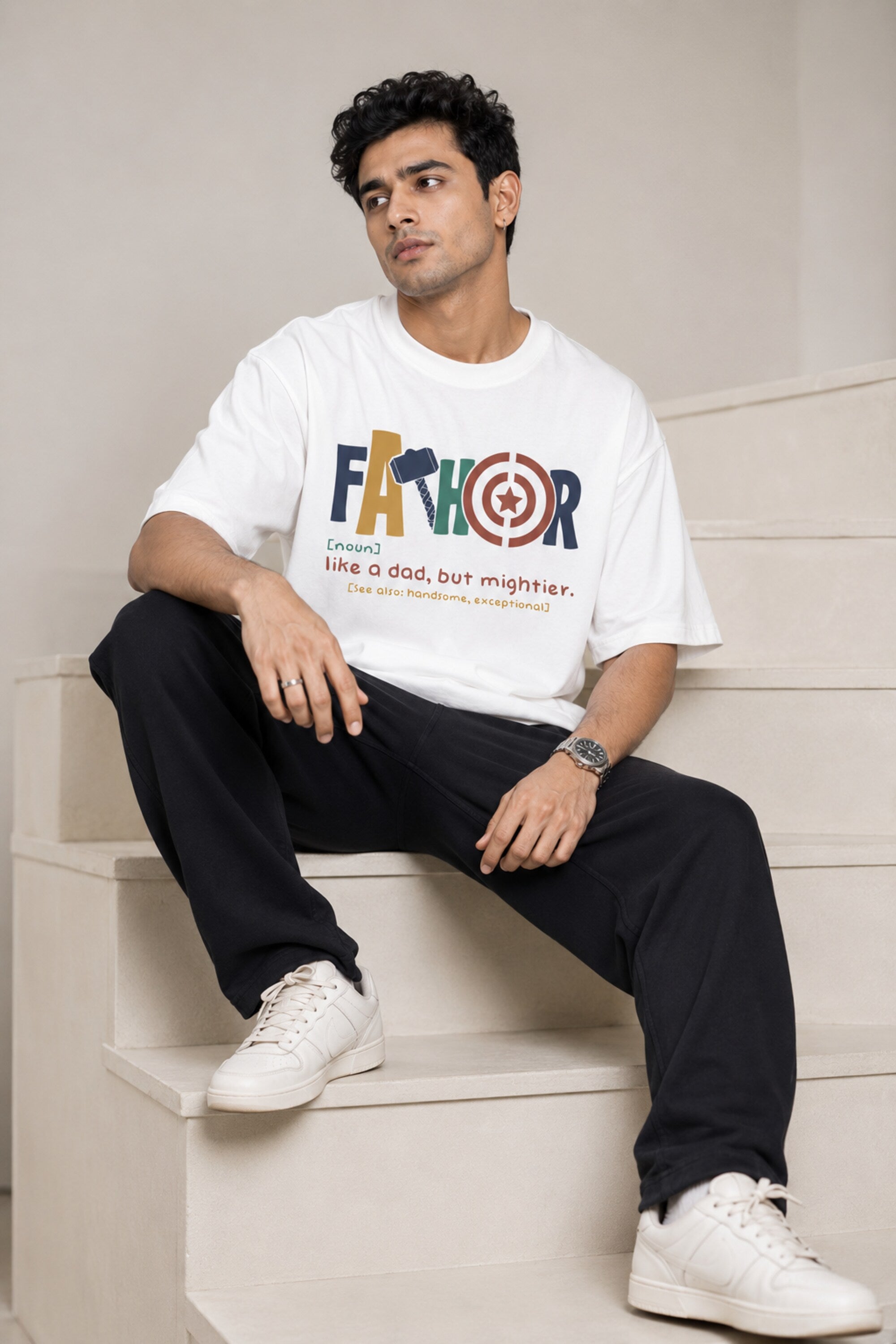 Man wearing a white oversized FAKR t-shirt with a graphic design of the word "Fakr" integrated with superhero symbols, on a plain gray background.