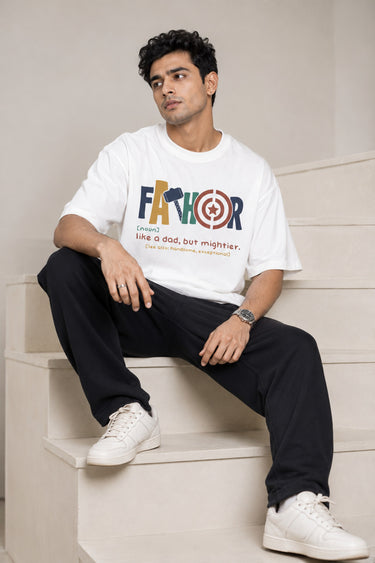 Man wearing a white oversized FAKR t-shirt with a graphic design of the word "Fakr" integrated with superhero symbols, on a plain gray background.