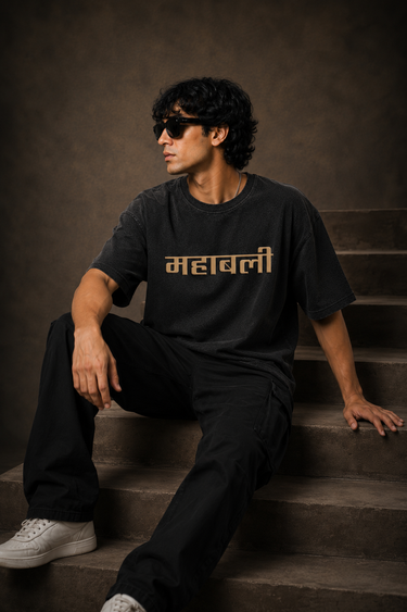 Man wearing an anthracite black 85-DENIM oversized t-shirt featuring a vibrant Hanumanji graphic print and Hindi text 'Mahabali' on the back. Styled for streetwear.