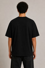 Black oversized t-shirt with the Hogwarts crest and 'Hogwarts' text in yellow, worn by a person. Features detailed coat of arms with lions, snakes, badgers, and eagles.