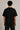 Black oversized t-shirt with the Hogwarts crest and 'Hogwarts' text in yellow, worn by a person. Features detailed coat of arms with lions, snakes, badgers, and eagles.
