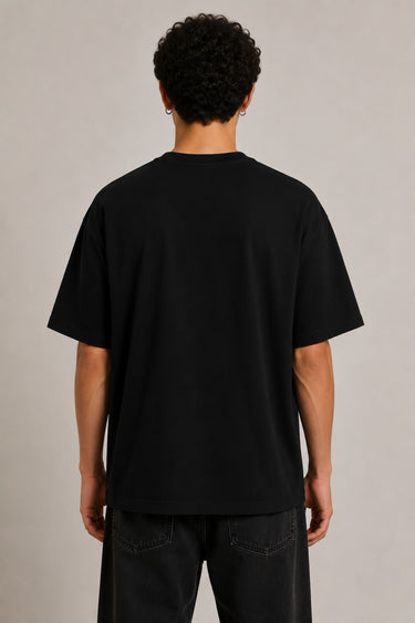 Black oversized t-shirt with the Hogwarts crest and 'Hogwarts' text in yellow, worn by a person. Features detailed coat of arms with lions, snakes, badgers, and eagles.