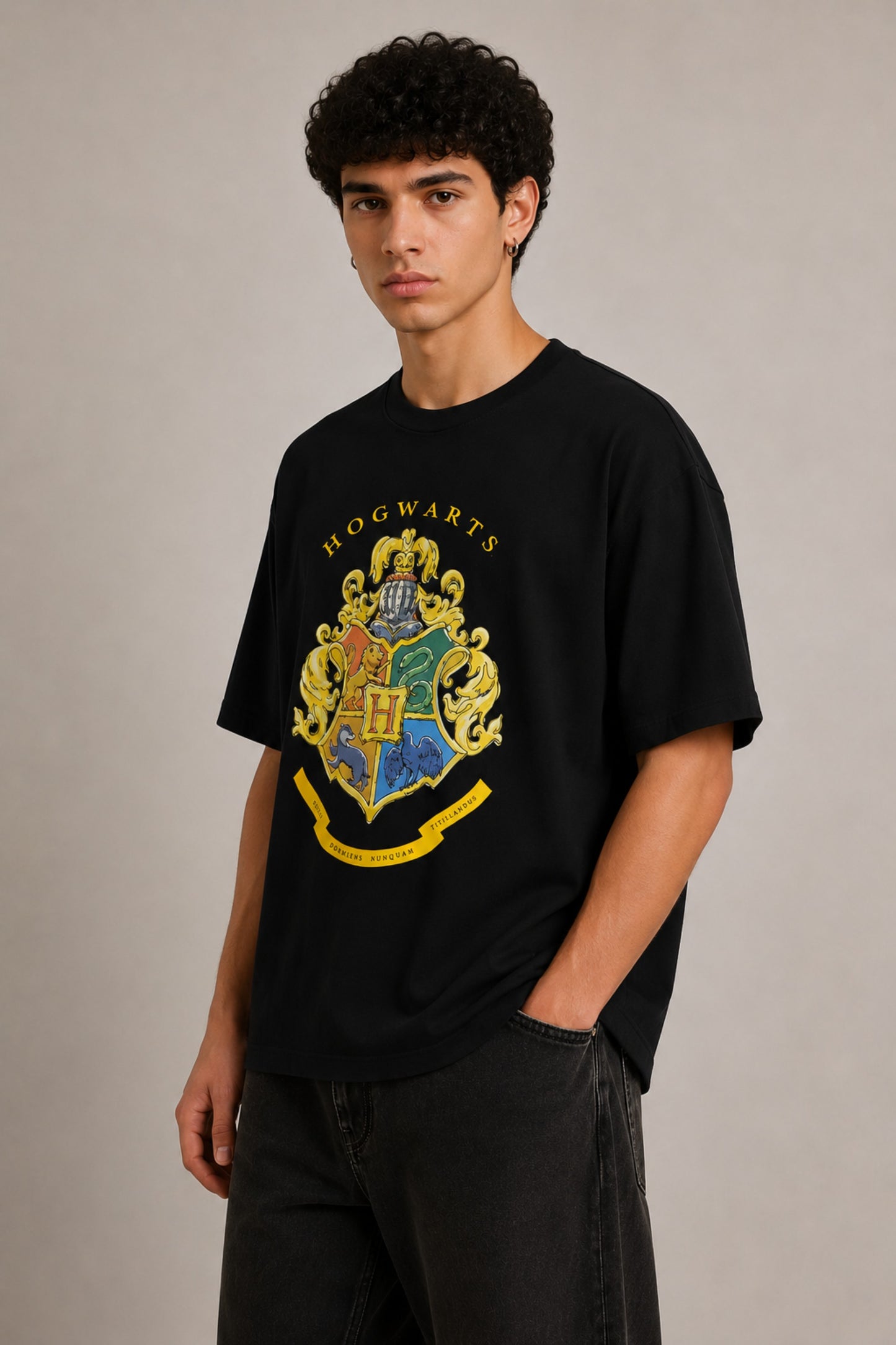 Black oversized t-shirt with the Hogwarts crest and 'Hogwarts' text in yellow, worn by a person. Features detailed coat of arms with lions, snakes, badgers, and eagles.