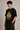 Black oversized t-shirt with the Hogwarts crest and 'Hogwarts' text in yellow, worn by a person. Features detailed coat of arms with lions, snakes, badgers, and eagles.