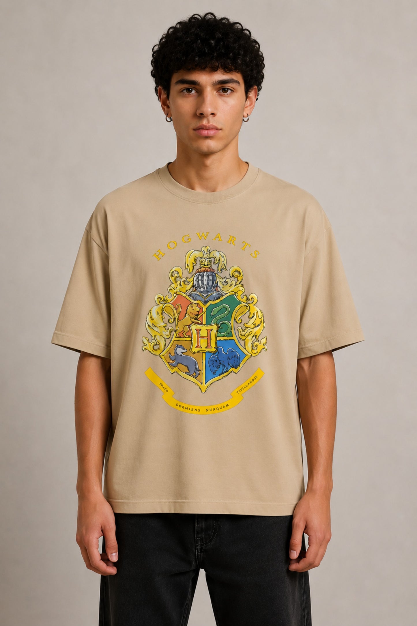 Black oversized t-shirt with the Hogwarts crest and 'Hogwarts' text in yellow, worn by a person. Features detailed coat of arms with lions, snakes, badgers, and eagles. - beige
