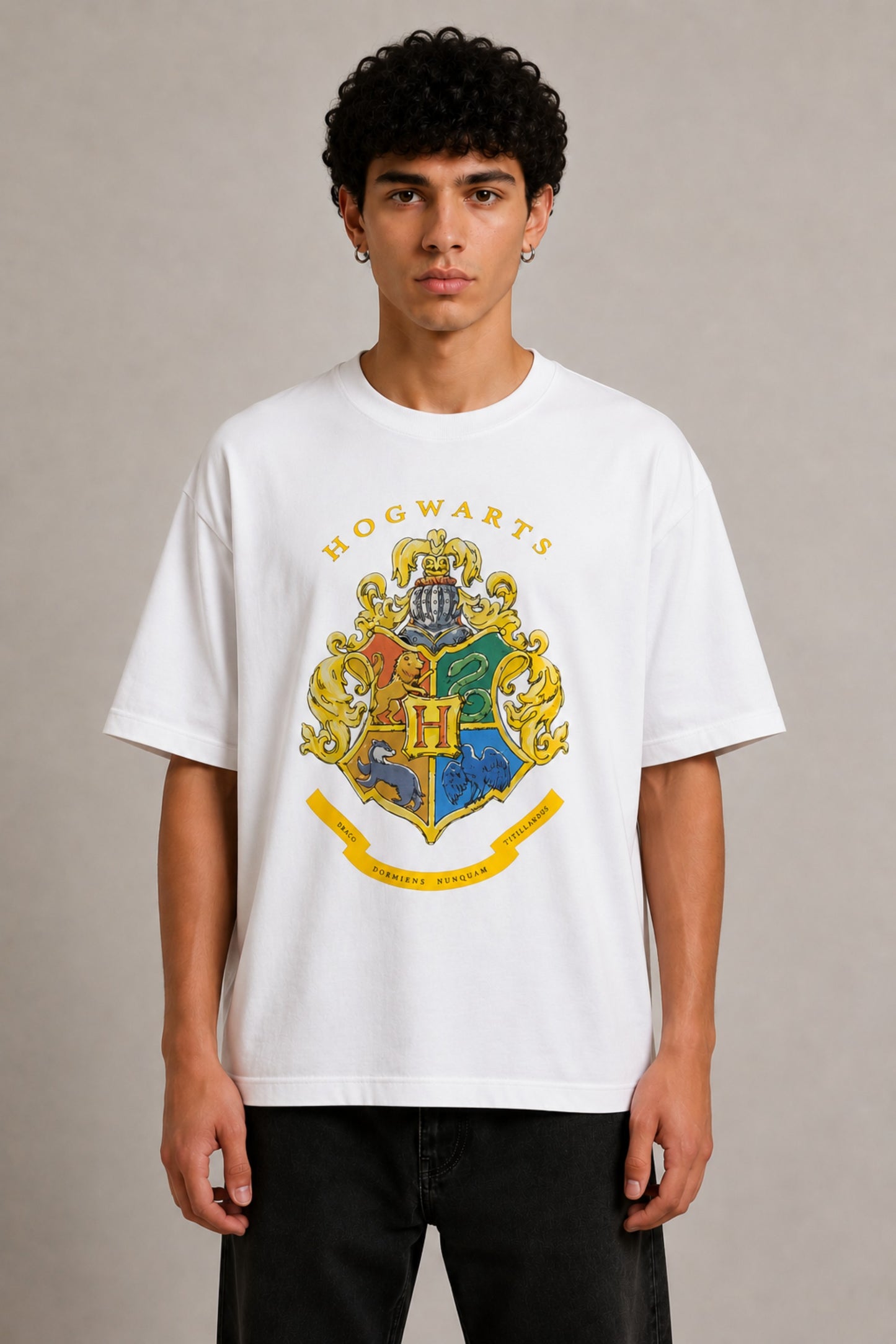 Black oversized t-shirt with the Hogwarts crest and 'Hogwarts' text in yellow, worn by a person. Features detailed coat of arms with lions, snakes, badgers, and eagles. - white