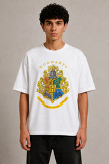 Black oversized t-shirt with the Hogwarts crest and 'Hogwarts' text in yellow, worn by a person. Features detailed coat of arms with lions, snakes, badgers, and eagles. - white