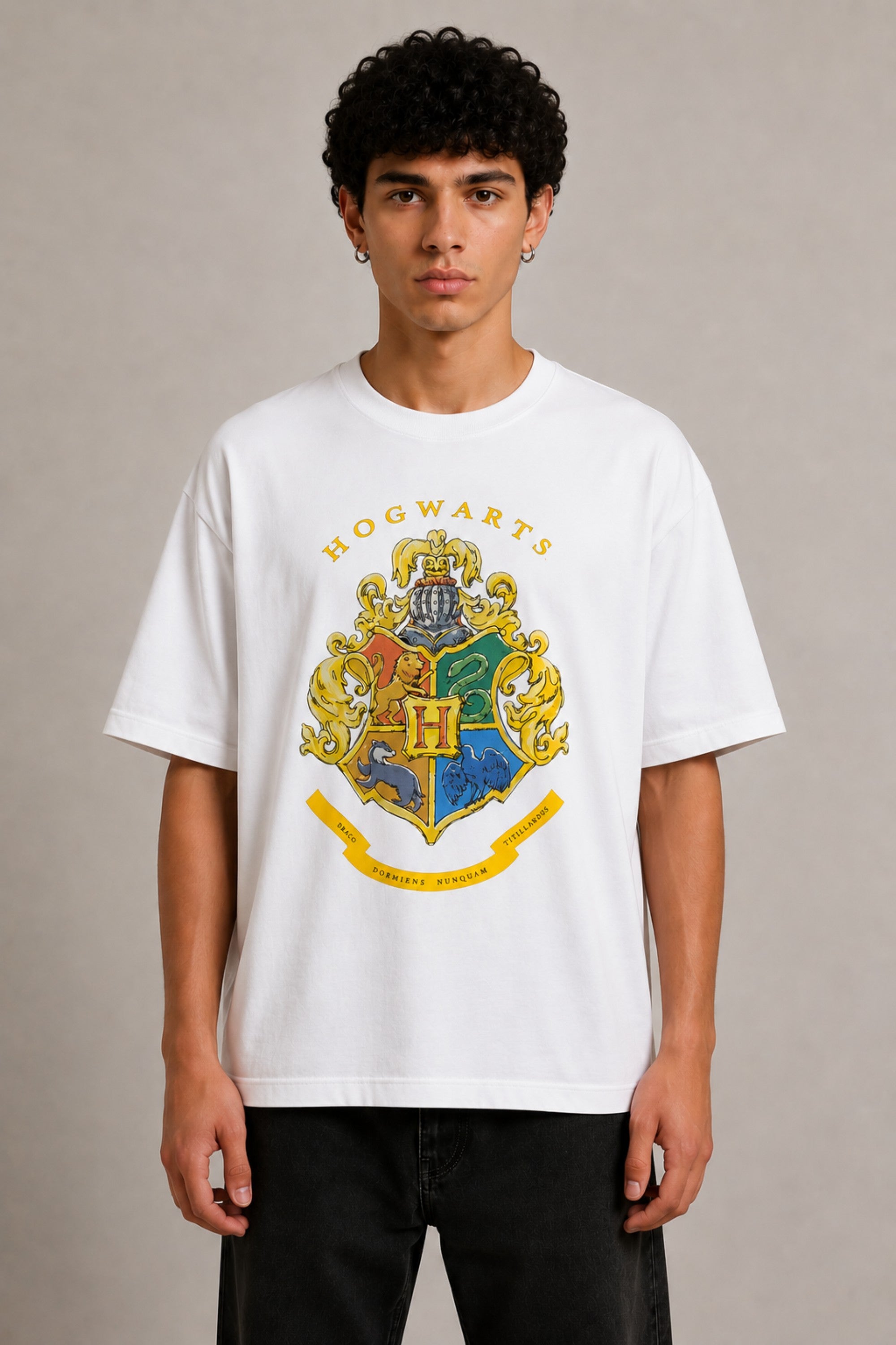 Black oversized t-shirt with the Hogwarts crest and 'Hogwarts' text in yellow, worn by a person. Features detailed coat of arms with lions, snakes, badgers, and eagles. - white