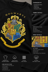 Black oversized t-shirt with the Hogwarts crest and 'Hogwarts' text in yellow, worn by a person. Features detailed coat of arms with lions, snakes, badgers, and eagles. - black