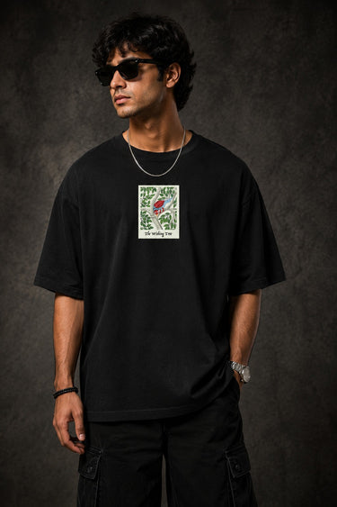 Man wearing a black Kalpvruksh oversized t-shirt with a colorful tree and bird graphic print on the back. Features Hindi script and 'The Wishing Tree' text. Streetwear style.