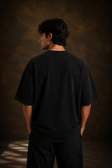 Model wearing a black KARMA oversized t-shirt with a golden sun graphic and the Sanskrit phrase 'कर्मण्येवाधिकारस्ते' (Your right is to action alone).