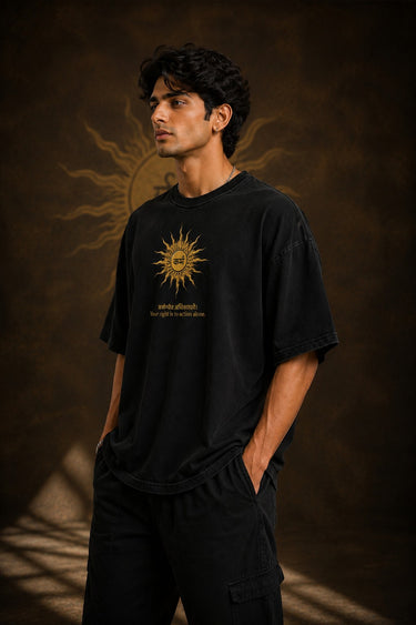 Model wearing a black KARMA oversized t-shirt with a golden sun graphic and the Sanskrit phrase 'कर्मण्येवाधिकारस्ते' (Your right is to action alone).