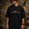 Man wearing a black KARNA oversized t-shirt with a sun graphic and Sanskrit text. Streetwear style, premium cotton feel.