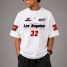 Back view of a man wearing a white LA 32 Drive oversized t-shirt with black text graphic. Model wears black cargo pants. - white