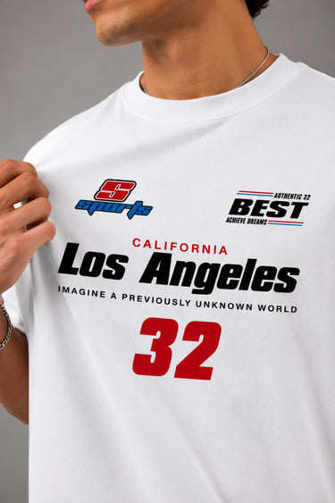 Back view of a man wearing a white LA 32 Drive oversized t-shirt with black text graphic. Model wears black cargo pants.