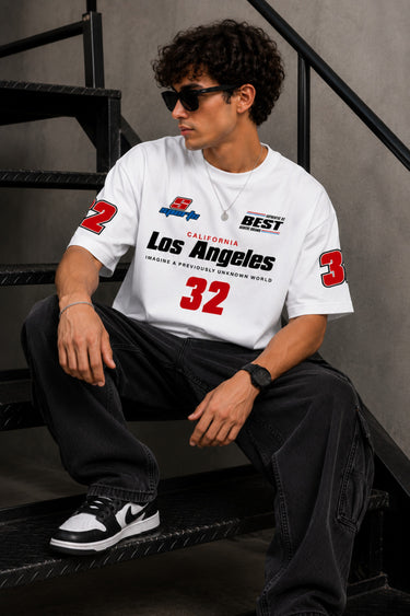 Back view of a man wearing a white LA 32 Drive oversized t-shirt with black text graphic. Model wears black cargo pants.