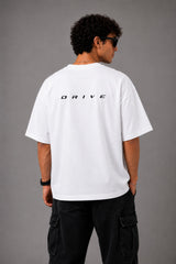 Back view of a man wearing a white LA 32 Drive oversized t-shirt with black text graphic. Model wears black cargo pants.