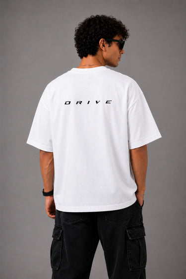 Back view of a man wearing a white LA 32 Drive oversized t-shirt with black text graphic. Model wears black cargo pants.
