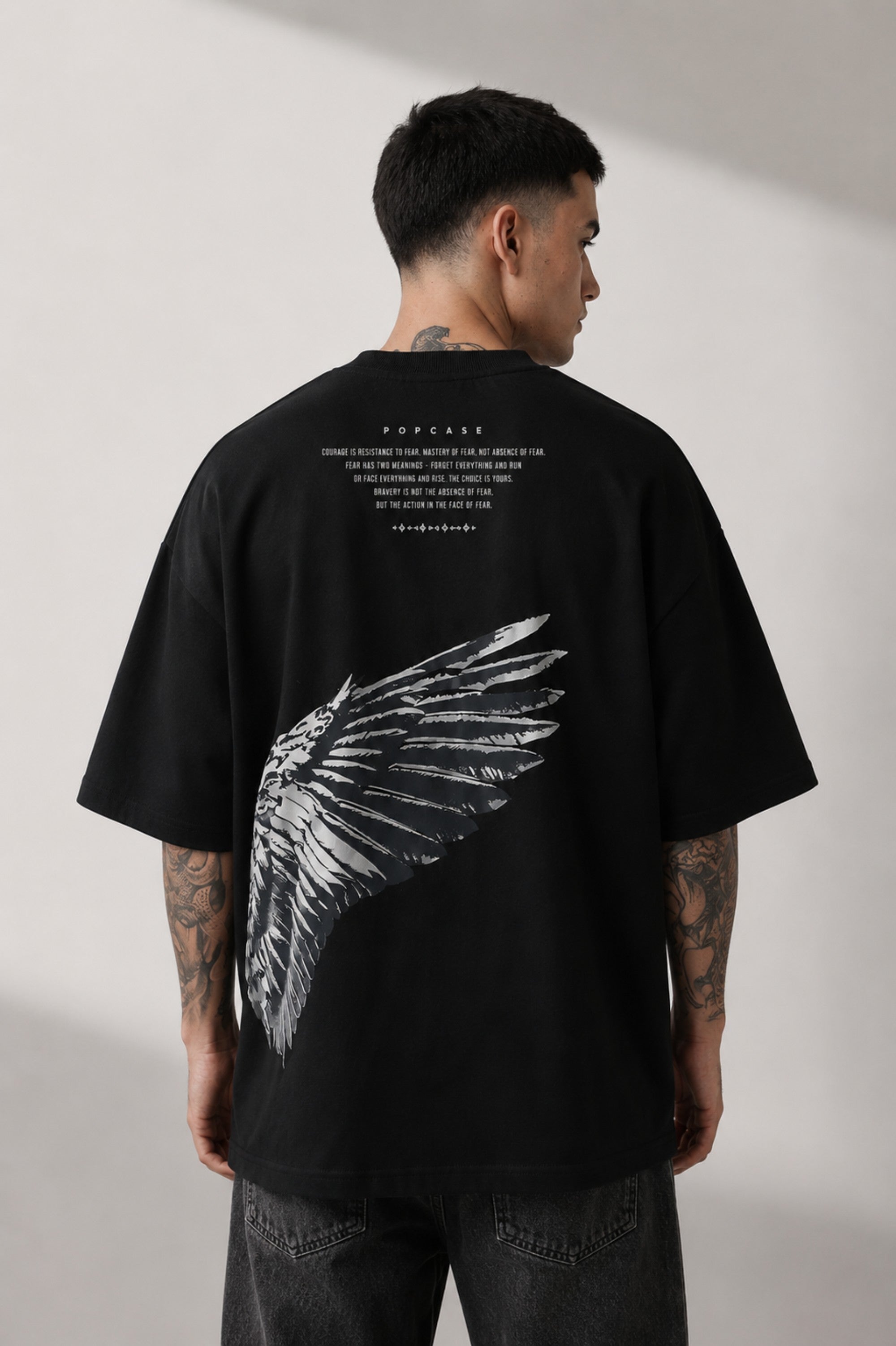 Black POPCASE LAUNCH oversized t-shirt featuring a large, distressed gray wing graphic print. Close-up on the premium fabric and detailed print for a streetwear aesthetic. - black