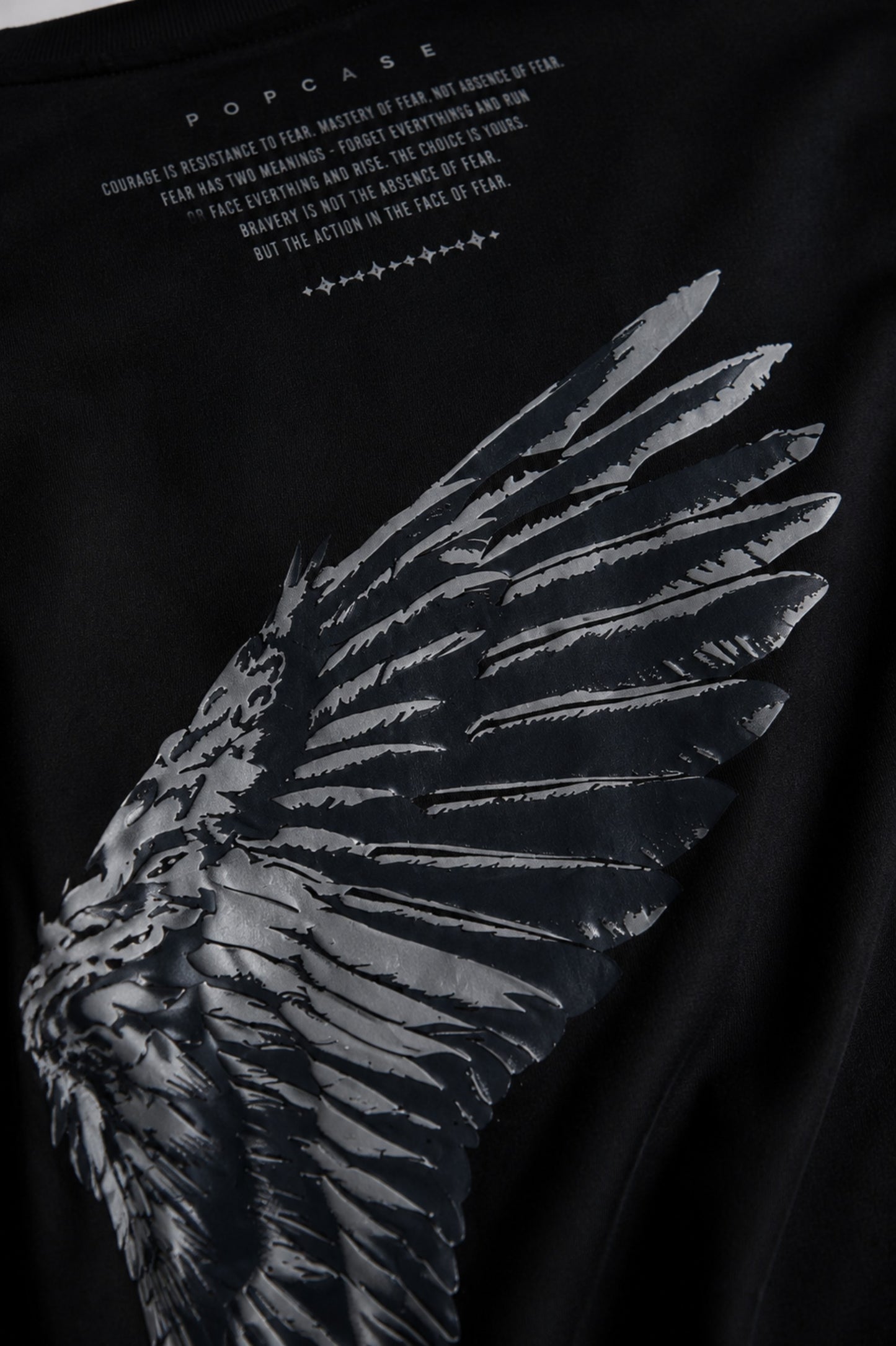 Black POPCASE LAUNCH oversized t-shirt featuring a large, distressed gray wing graphic print. Close-up on the premium fabric and detailed print for a streetwear aesthetic.