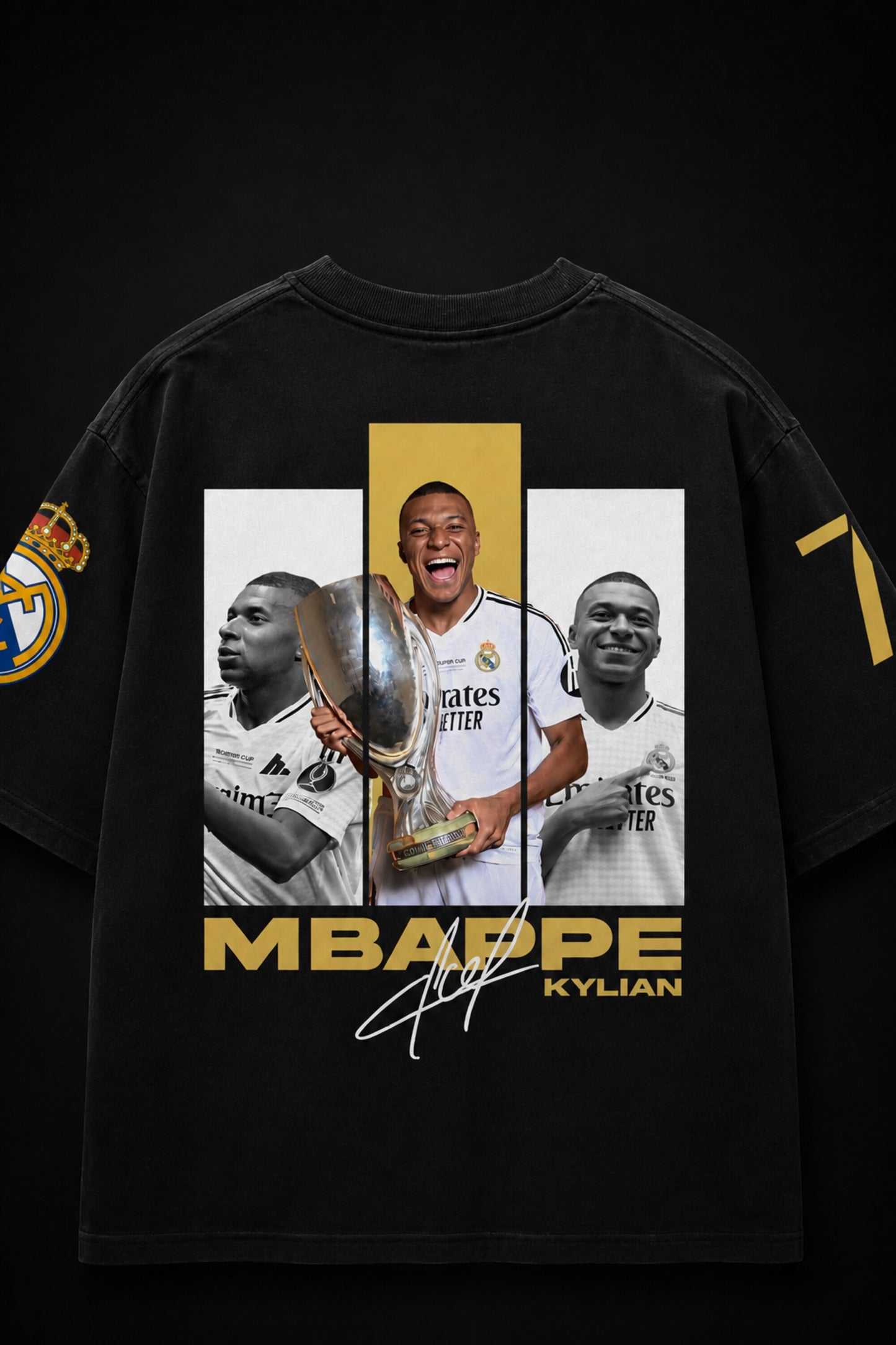 A black graphic t-shirt featuring a large print of footballer Kylian Mbappé in a Real Madrid jersey, holding a trophy, with 'MBAPPE KYLIAN' and a signature on the front. The t-shirt also has a Real Madrid crest on the sleeve and a gold number 7 on the other sleeve.