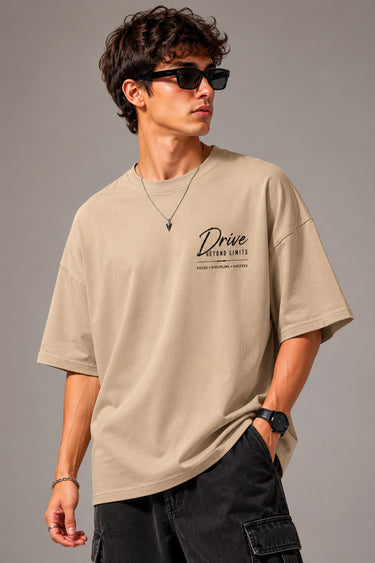 Man wearing a tan oversized t-shirt with a graphic print of the McLaren Senna car and "McLaren Senna" text. He is sitting on metal stairs.