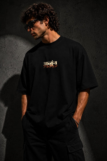 Black MIGHTY ARJUN oversized t-shirt featuring distressed Hindi script graphic in beige and orange, highlighting streetwear style.