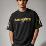 Model wearing an anthracite black Mbappe oversized t-shirt with gold "MBAPPE" graphic and signature, Real Madrid and number 7 logos on sleeves.