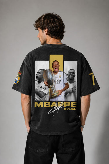 Model wearing an anthracite black Mbappe oversized t-shirt with gold "MBAPPE" graphic and signature, Real Madrid and number 7 logos on sleeves. - anthracite black