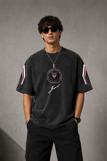 Man wearing an anthracite black Messi oversized t-shirt with a circular team logo and signature, showcasing the relaxed fit and premium fabric.