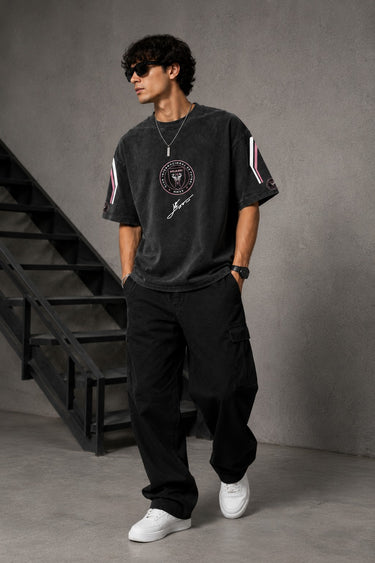 Man wearing an anthracite black Messi oversized t-shirt with a circular team logo and signature, showcasing the relaxed fit and premium fabric.