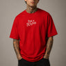 Model wearing a red oversized t-shirt with 'Just a 90's Kid' graphic. The tee has a relaxed fit, paired with black jeans and white sneakers, embodying a retro streetwear style. - red