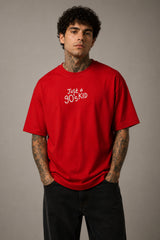 Model wearing a red oversized t-shirt with 'Just a 90's Kid' graphic. The tee has a relaxed fit, paired with black jeans and white sneakers, embodying a retro streetwear style. - red