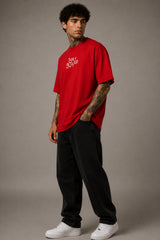 Model wearing a red oversized t-shirt with 'Just a 90's Kid' graphic. The tee has a relaxed fit, paired with black jeans and white sneakers, embodying a retro streetwear style.