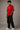 Model wearing a red oversized t-shirt with 'Just a 90's Kid' graphic. The tee has a relaxed fit, paired with black jeans and white sneakers, embodying a retro streetwear style.