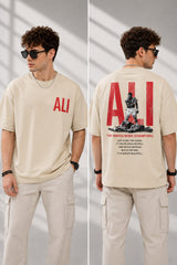 Man wearing a white ALI oversized t-shirt and beige cargo pants, sitting on grey stairs. He wears black sunglasses and jewelry. - beige