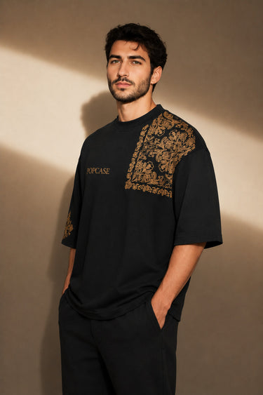 Back view of a person wearing a black ART ON OVERSIZED TSHIRT with gold embroidered detail on the left sleeve. Shows the oversized fit and premium streetwear aesthetic.
