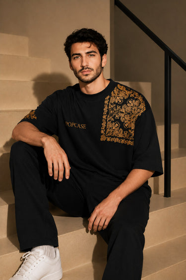 Back view of a person wearing a black ART ON OVERSIZED TSHIRT with gold embroidered detail on the left sleeve. Shows the oversized fit and premium streetwear aesthetic.