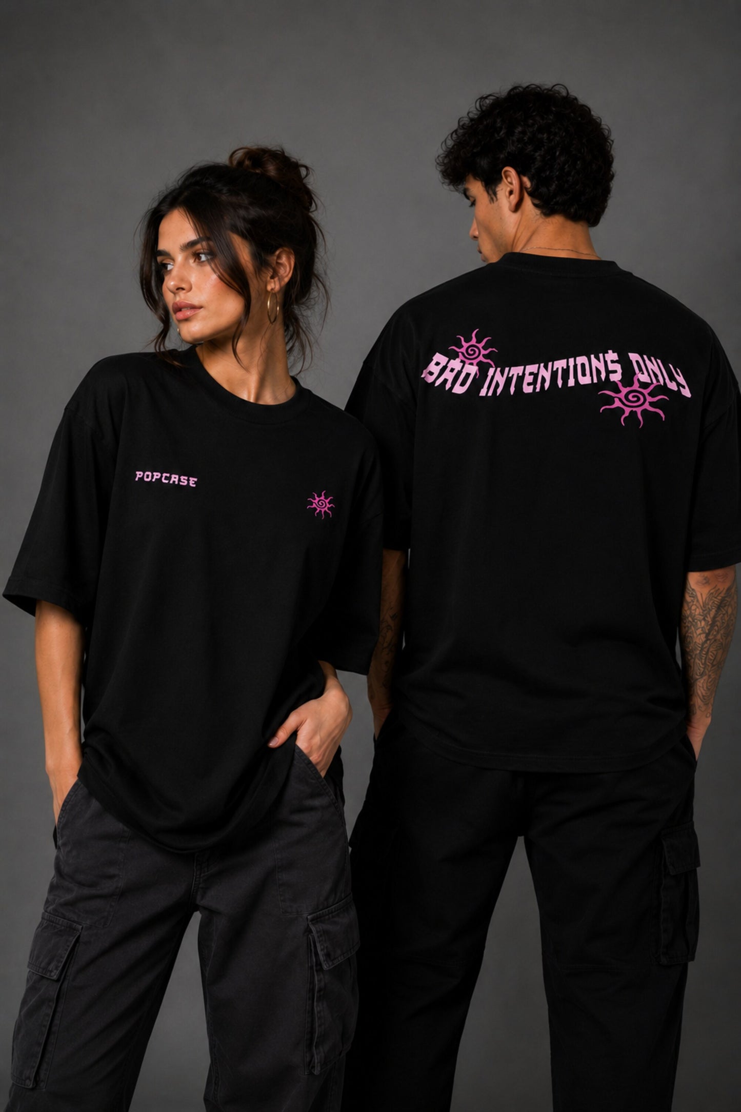 Black POPCASE oversized tshirt with Bad Intentions Only pink gothic text and tribal sun print on back, worn with black cargo pants