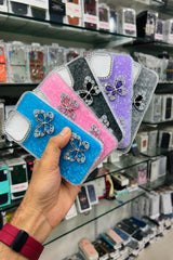Hand holding a stack of embellished phone cases with a store shelf in the background.