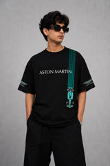 Man wearing a black Aston Martin oversized t-shirt with green racing stripes and the iconic Aston Martin wings logo, sitting on industrial stairs.