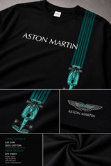 Man wearing a black Aston Martin oversized t-shirt with green racing stripes and the iconic Aston Martin wings logo, sitting on industrial stairs.